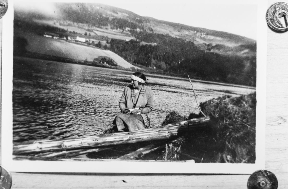 Ukjent kvinne ved vann, eller elv, gårdsbruk i lia på den andre siden