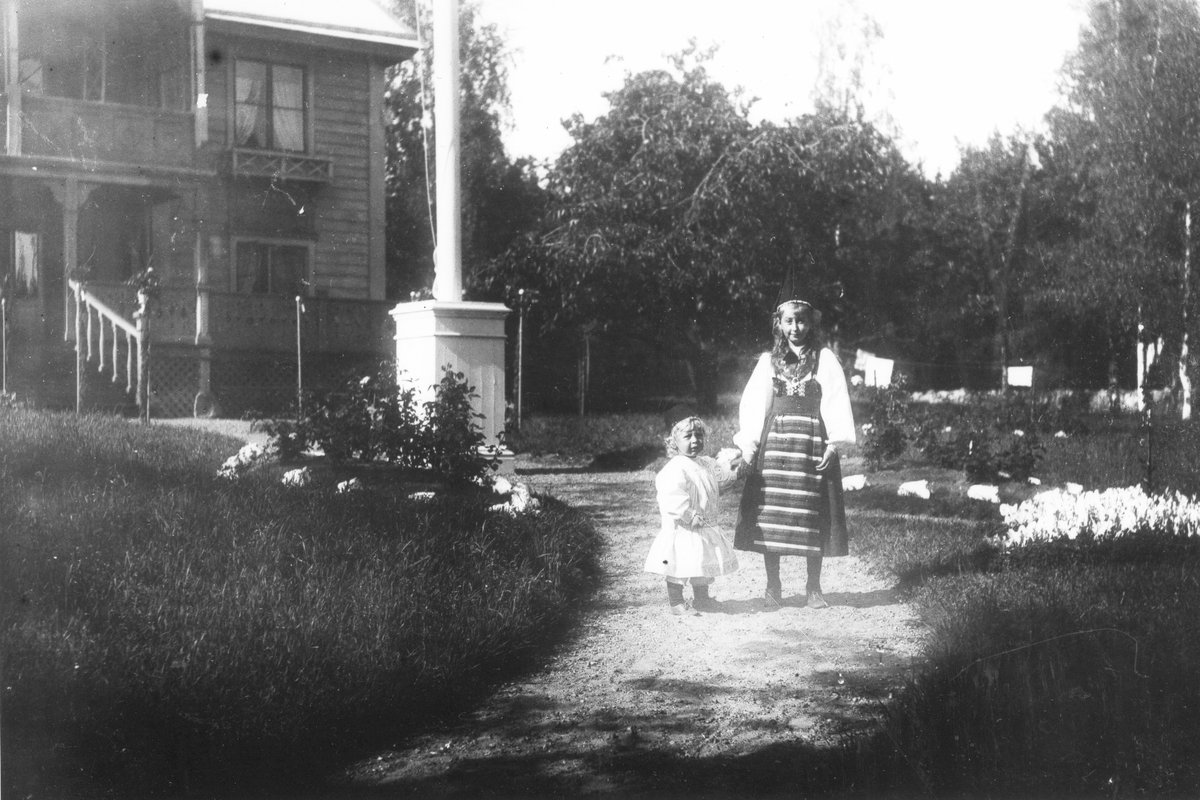 Två flickor på gården utanför sommarhuset Gröndal 1897, klädda i folkdräket.
