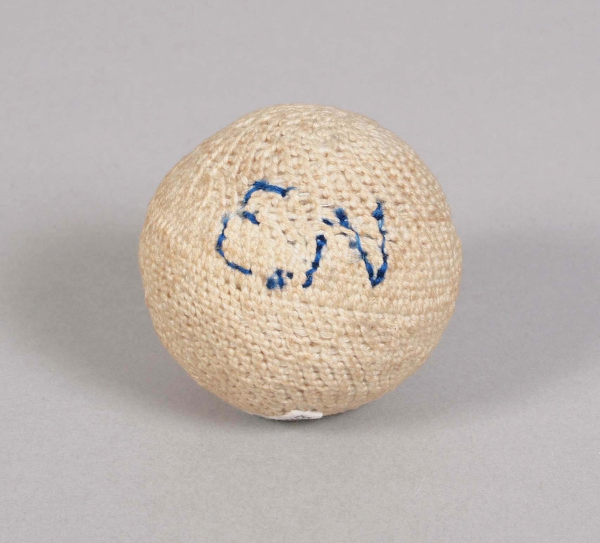 Boll med stickat ytterhölje av benvitt bomullsgarn. Söm på mitten. Märkt: "E.N" i blått garn. Stoppning av vitt garn.