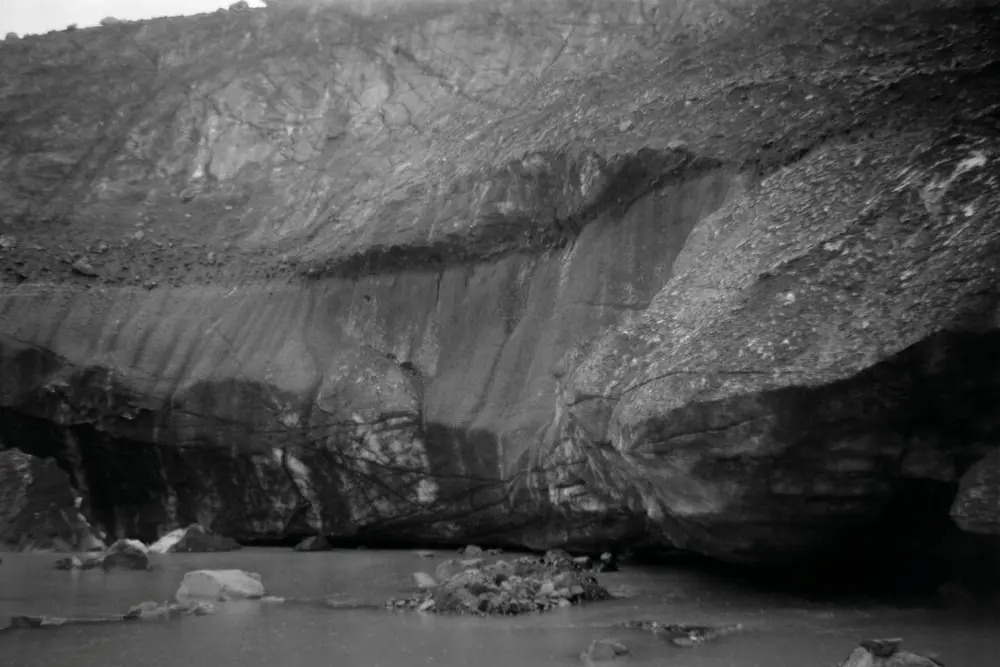 Black and white image of a steep rock wall ending in water. It looks like it's raining. The photograph is a little blurry.