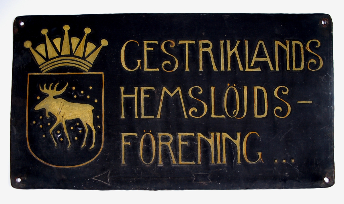 Skylt, Gestriklands hemslöjdsförening, tillsammans med Gästriklands vapen. Svart botten, text i guld.