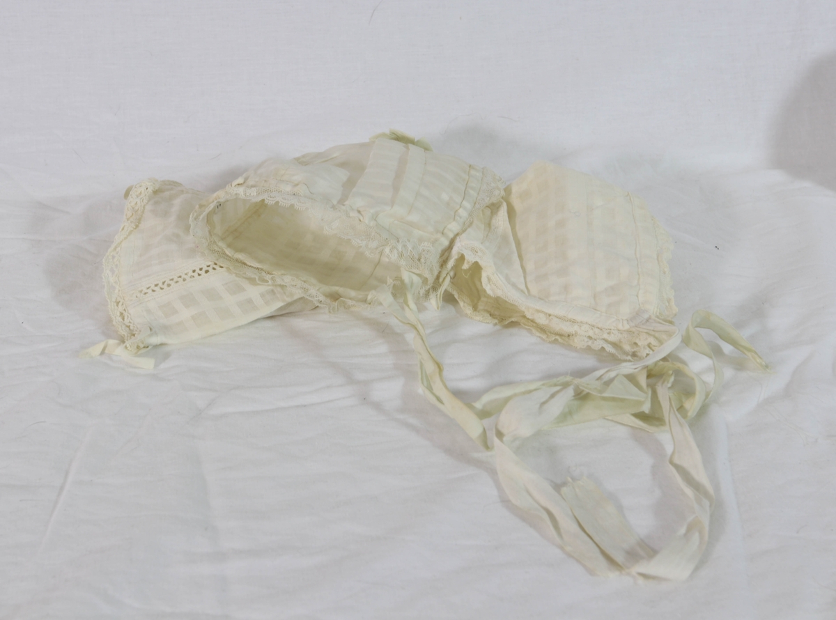 Trekantformede hvite tøystykker, dekorert med silkebånd og blondeborder