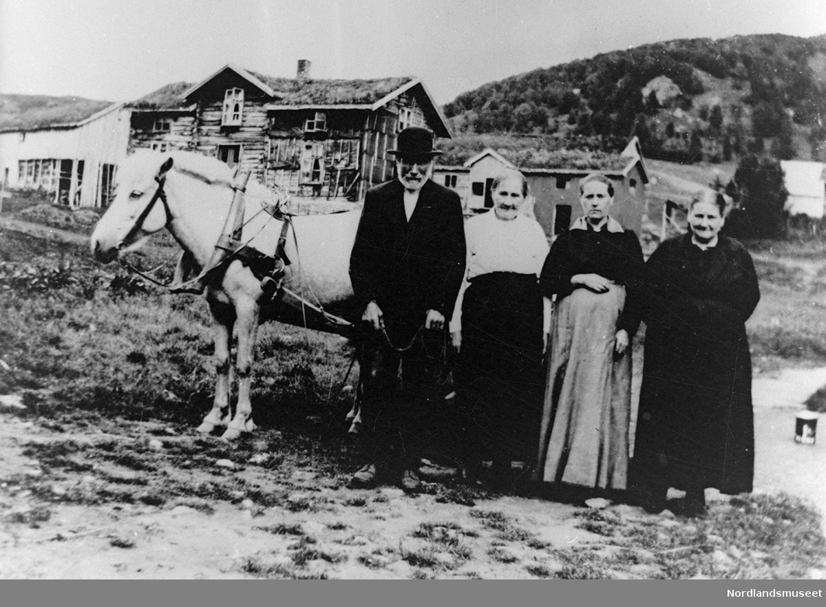 En eldre mann, tre eldre kvinner står foran en hest og vogn. I bakgrunnen bebyggelse i Skar (misjonsbasar). Fra venstre: Anders Skar, Karoline, Anna Hansen og Elise Skar.