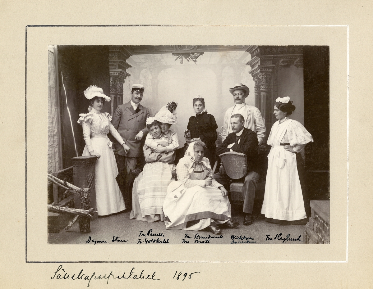 "Sällskapsspektakel 1895". 
Ett sällskap som spelar amatörteater har samlats hos fotografen.
Fr.v.: "Dagmar..., Sture..., fru Perselli, fr. Goldkuhl, fru Strandmark, fru Bratt, Wickbom, Dahlström, fru
Haglund".