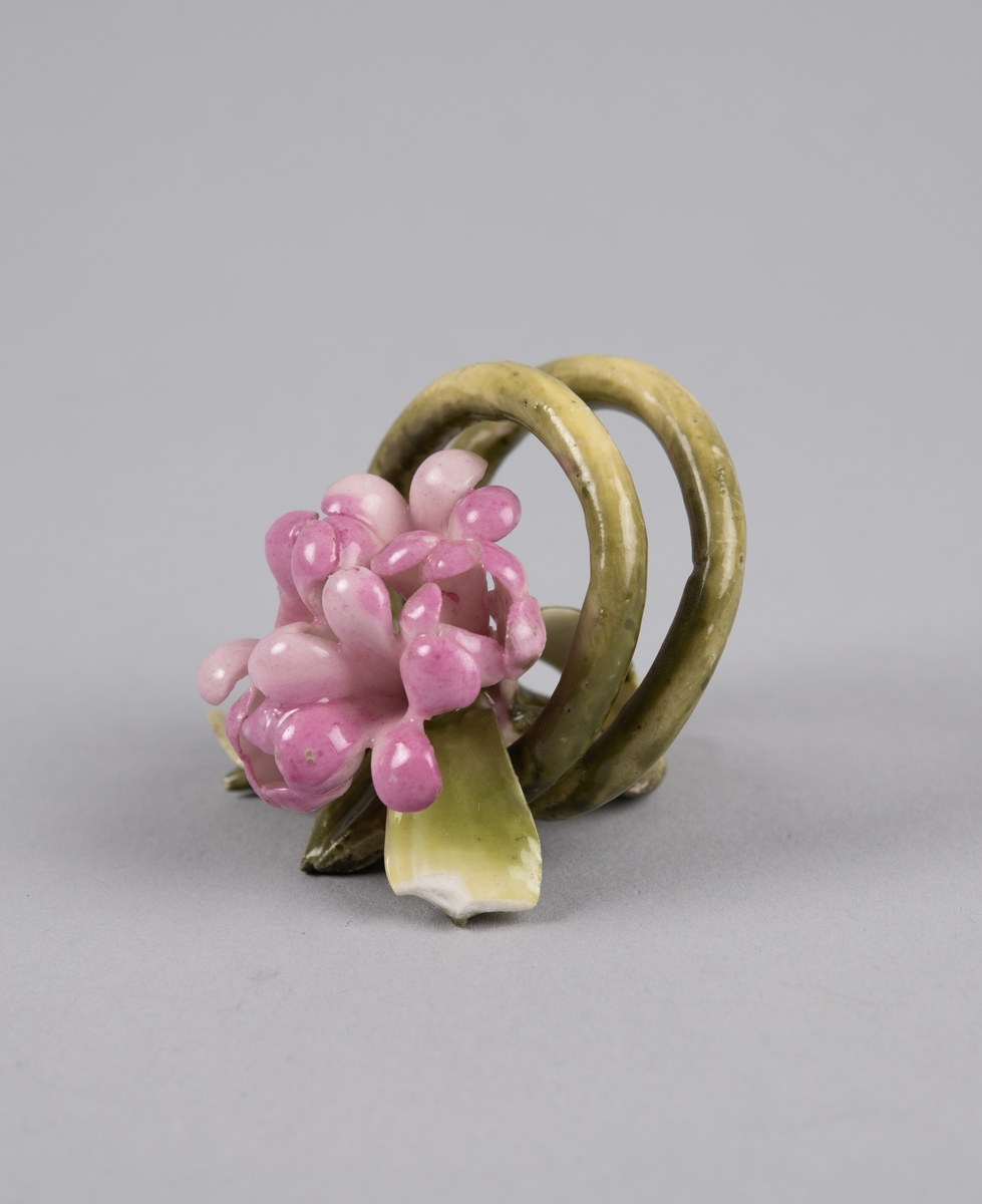 Modellert blomst til borddekor. Stilken danner to ringer som fungerer som en holder til kort eller serviett.
