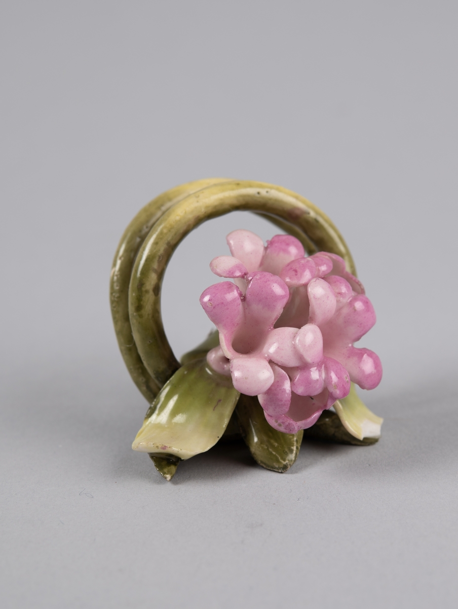 Modellert blomst til borddekor. Stilken danner to ringer som fungerer som en holder til kort eller serviett.
