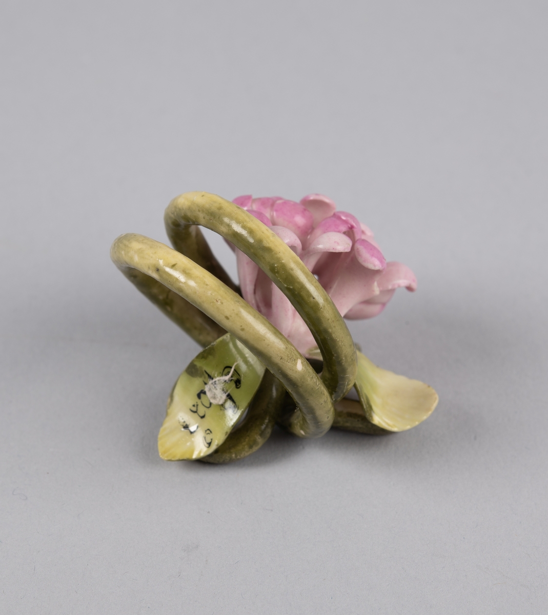 Modellert blomst til borddekor. Stilken danner to ringer som fungerer som en holder til kort eller serviett.
