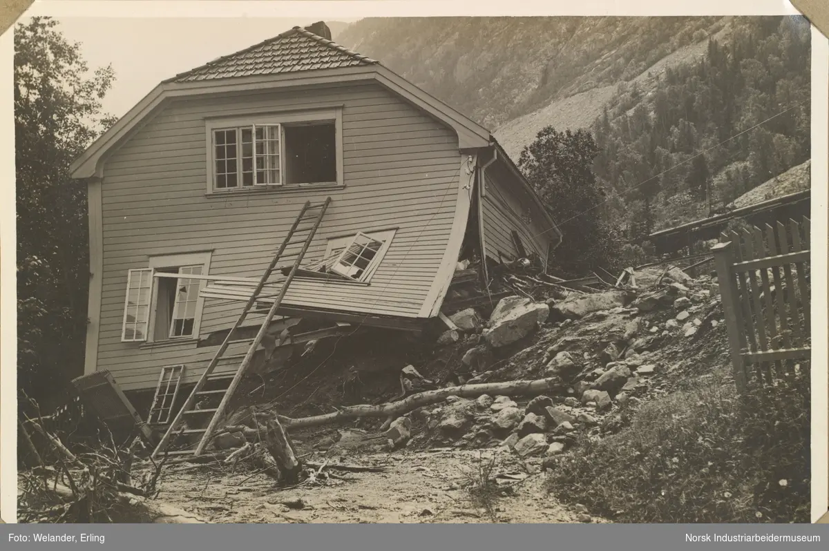 Ødeleggelser etter flommen på Rjukan 28.-29. juni 1927. Bolighus total ødelagt etter ras øst for Rjukan stasjon. Stige er satt opp til husveggen og opp i vindu i andre etasje. Bolighus av type J (Flekkebyhus).