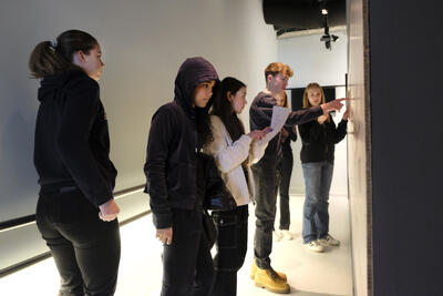 Elever ser mot en vegg der det henger informasjon. De har papir og penner i hendene.