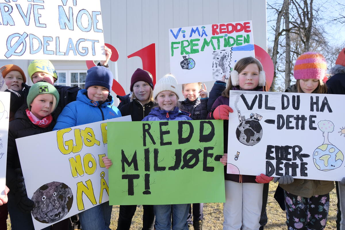 En gruppe elever har plakater med slagord for et bedre klima, de er kledd i vinterklær. Bildet er tatt utenfor Eidsvollsbygningen