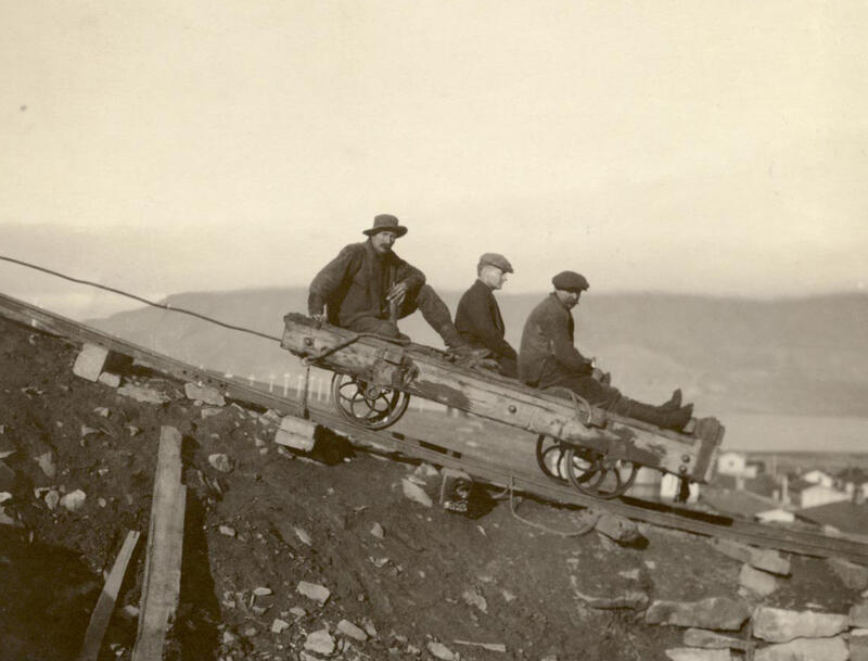 Tre menn på vei ned fra fjellet i vogn på skinner.