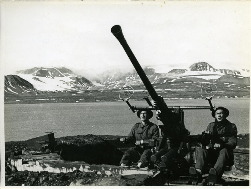 To menn som betjener en luftvernskanon. Fjord og snødekte fjell i bakgrunnen.
