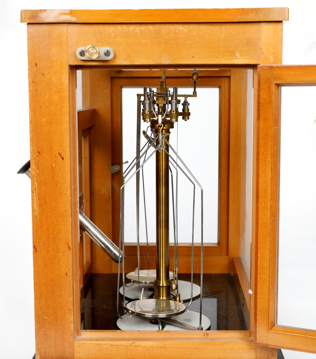 Analysevekt montert i trekasse med glass. Dører foran og på hver side. Glass i vegger, dører og tak. Mikroskop på midten foran.