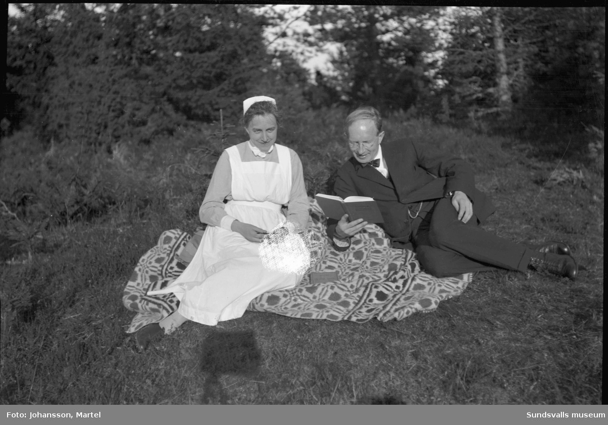 Fotografen Martel Johansson sitter på en filt i gräset tillsammans med en kvinna i sköterskeuniform.