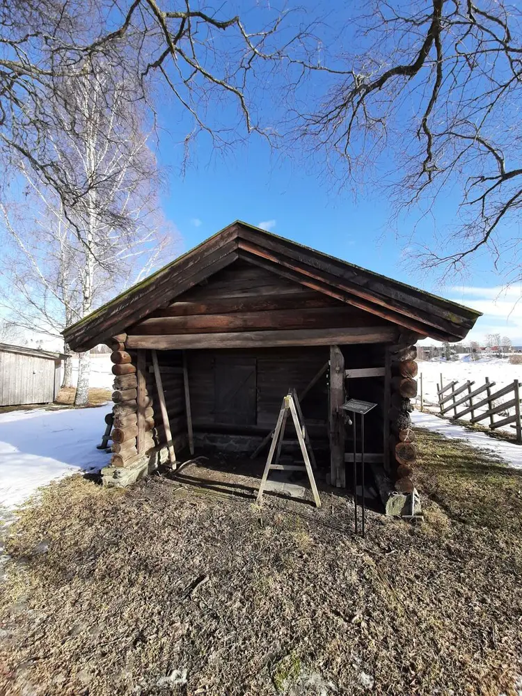 Bildet viser en eldre lintørke. Huset er laftet. Det er snø på bakken.