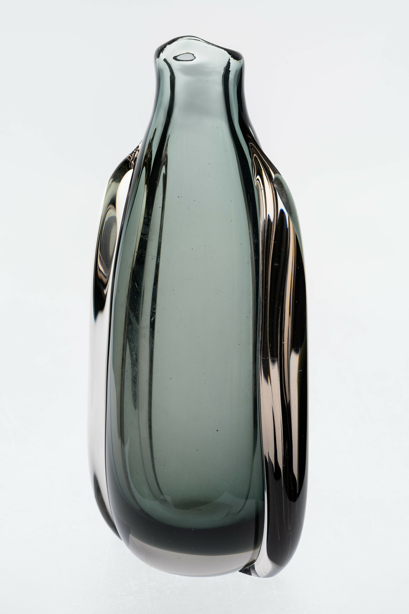 Vase i gjennomskinnelig glass. Sylinderformet gråfarget korpus med kort hals som ender i et nebb. Vasens skulpturelle utforming alluderer til en pingvin.