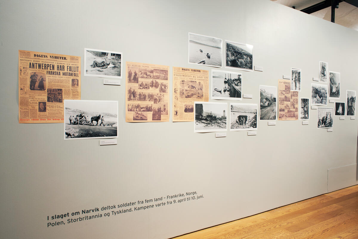 Exhibition wall with newspaper clippings and photographs mounted close together.