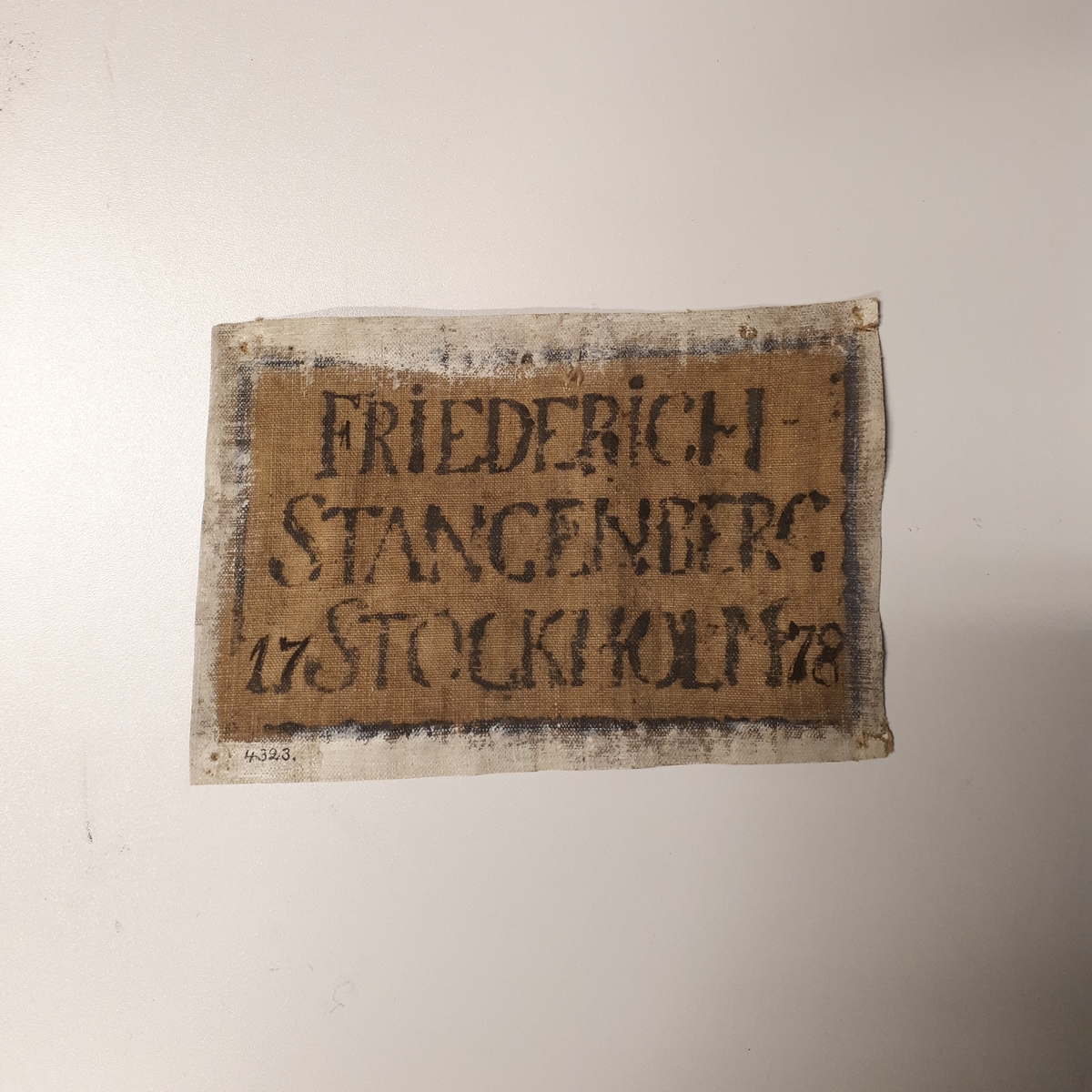 Rektangulär bit av en segelduk med tryckt text i svartblått: "Friedrich  Stangenberg 17 Stockholm 78”  inom fyrkant.