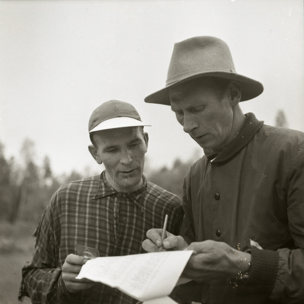 Två män läser en lista under distriktsmästerskap i orientering vid Trönö den 26 september 1954.