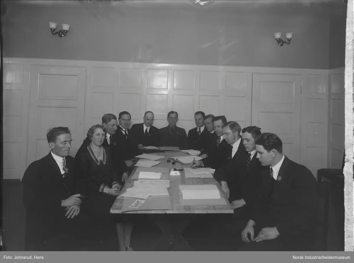 Snøggs hovedstyre, elleve menn og en kvinne, sittende rundt et bord dekket med dokumenter. Midt på bordet står ett askebeger med en pipe liggende oppi.