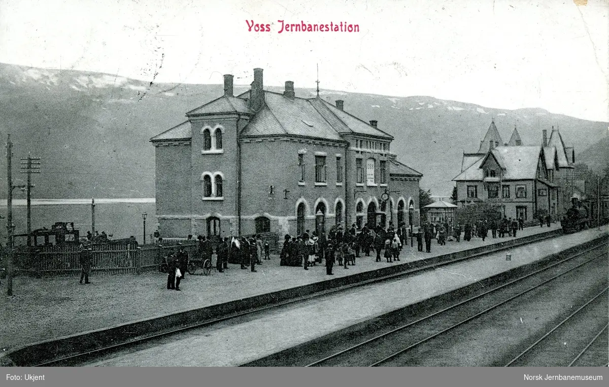 Voss stasjon. Mange reisende på plattformen idet tog fra Bergen kjører inn på stasjonen