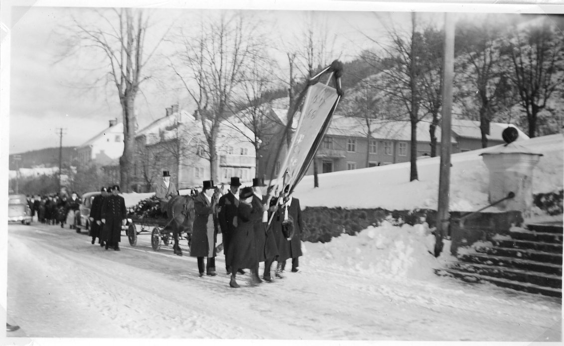 Ett begravningståg på Brahegatan i Gränna nedanför kyrkan. Det är vinter med snö.