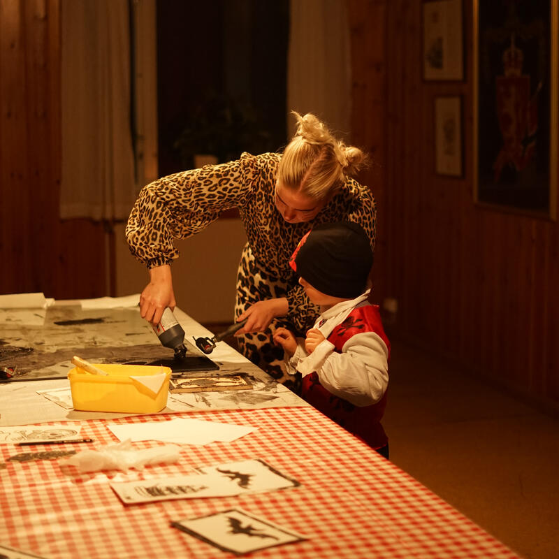 En kvinne hjelper et barn med å trykke halloweenmotiver på papir.