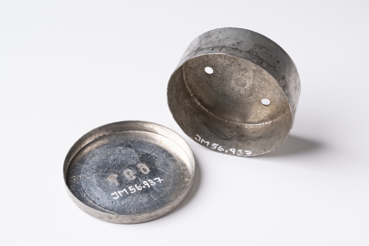 Lönedosa av metall, rund med lock. På locket är präglat nummer "697". Dosans botten har stansade hål.

Se vidare Historik.
