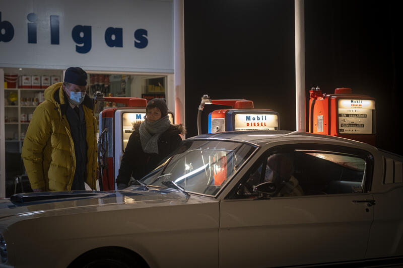 Bildet viser en bil og filmcrew foran en bensinstasjon under en filminspilling.