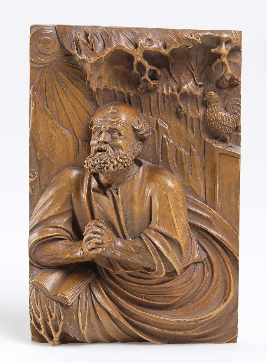 Bild av aposteln Petrus i bedjande ställning under ett träd, vid ena sidan en uppslagen bok, vid den andra sidan å upphöjd plats tuppen, Relief i trä