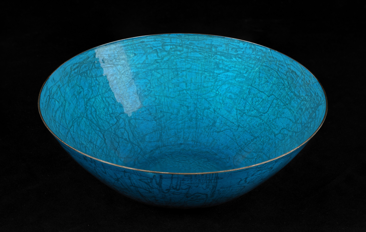Halvkuleformet skål i sølv, dekorert med transparent turkis og blåfarget kontraemalje. Freset dekor i form av kryssende geometriske linjer.