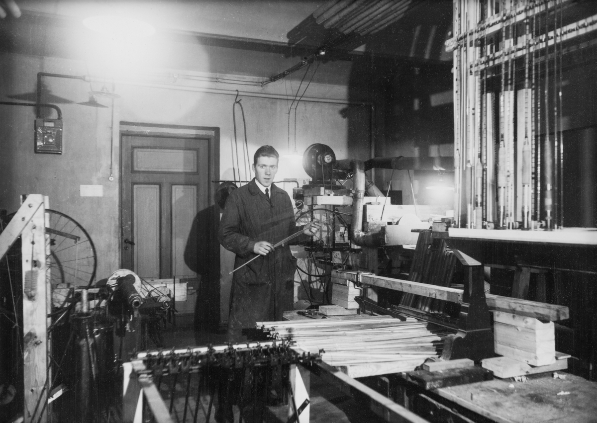 Fotografiet er tatt  i de første produksjonslokalene til Asbjørn Hørgård i kjelleren på Bispehaugen skole i Trondheim i 1935. Her ble det produsert laminerte fiskestenger, splitcanestanger, med utgangspunkt i bambus (tonkinbambus) som råemne. Asbjørn Hørgård (1910-2001) ses midt bildet der han holder spildrer av tonkinbambus i hendene. Hørgårds selvlagete maskiner for uthøvling av tokinspildrer (splitcanespildrer) ses også i bildet. (Se Hørgårds bok «Sportsfiske som hobby i 65 år», s. 4 der framstillingsmåten og maskinene beskrives.)

[Se referanser og referanser til filer for mer informasjon om hvordan framstillingen av splittkeinstenger foregikk. Se fanen «Opplysninger» for informasjon om Asbjørn Hørgård og hans firma. ]