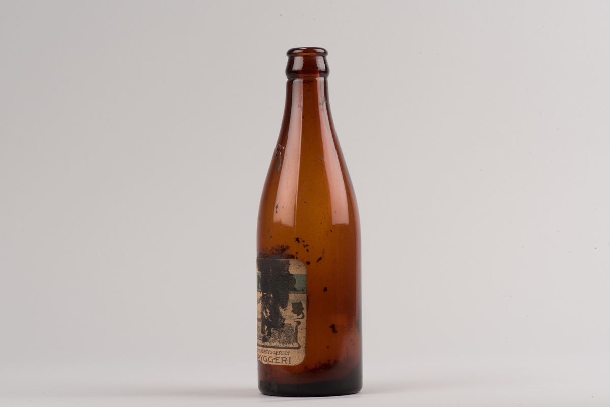 Pilsnerflaska i brunt glas.
På flaskan finns ett H omgivet av tre stiliserade blommor. En etikett med text och motiv visar att pilsnern var bryggd på Mjölby bryggeri. Motivet på etiketten är bryggeribyggnaden.