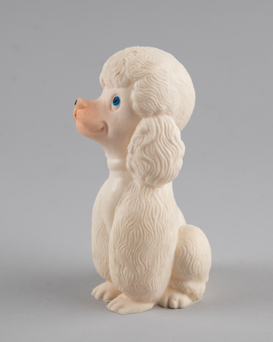 Leketøy av mykplast i form av en sittende hund, en puddel. Den er hvit med blåe øyer, svart snute og rød tunge.