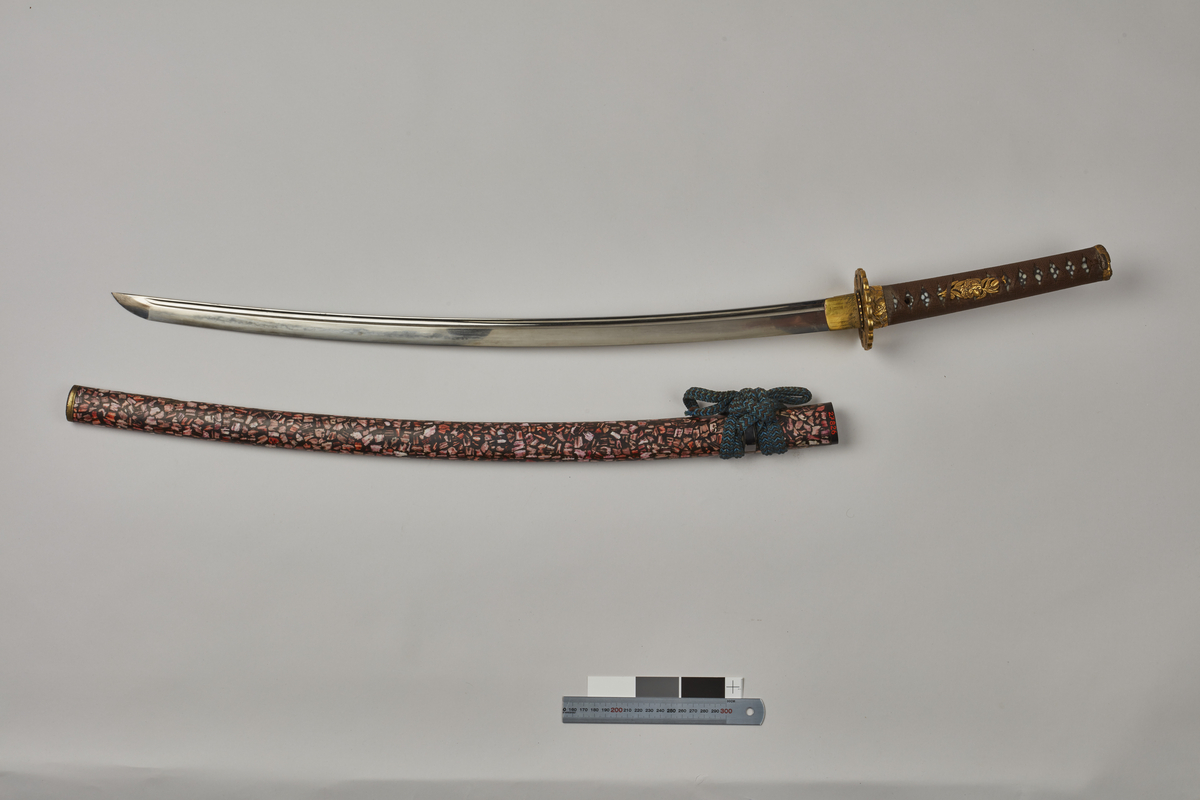 Per Terje Norheim juli 2019:
Pair of Japanese swords, daisho (litterally long-short).
Long sword dai, mounted as katana
Blade:
Total length 90,3 cm, length to ha-machi (notch at beginning of tang) 68,0 cm, width at ha-machi 3,0 cm.
Even curve with bohi (wide grove) all the way.
Hamon: (tempering) choji-ha (strong irregular, «clove like» line).
Nakago: (tang) suriage (shortened) 3 meguki ana (peg holes)
Mei: (signature) mumei (unsigned).
Fair condition.
Short sword wakizashi
Blade:
Total length 60,5 cm, length to ha-machi 47,0 cm, width at ha-machi 2,6 cm.
Even curve, no carvings
Hamon: (tempering) sugu midare-ha (straight with some irregularities)
Nakago: (tang) suriage (shortened) 2 mekugi ana (peg holes)
Mei: (signature) mumei (unsigned:
Good condition. 
Koshirae (mounting)
As both blades are mounted in a similar way the mounts are described for the pair as such.
Saya: (scabbards) completely covered in large pieces of shell. Kurikata (cord loop) black laquered.
In the wakizashi scabbard a kozuka (byknife)  decorated with the saga of Watanabe no Tsuna and the encounter at Rashomon gate.
Tsuba: (guards) in brass, shaped like flower heads, partly piereced (sugake).
Tsuka: (hilts) unusual. Instead of the ordinary white same (ray skin) the same has been covered in black laquer and then grinded down to a smooth surface.Over the same a wrapping of silk cord. All hilt mounts, i.e. fuchi-kashira (bottom and top mounts) of brass with extencive carving, slightly different on the two swords. On the katana leaves and praying mantis, on the wakizashi waves. Good quality. The fuchi on both with signature which is difficult to read but includes the information ..roku ju hachi nen, i.e 68 years (of age).
Both swords have 2 seppa(washers on both sides of tsuba) in brass with serrated edge.
The mounting as such is late Edo period. The blades are older, the dai probably late Koto, the sho most probably a bit later.
