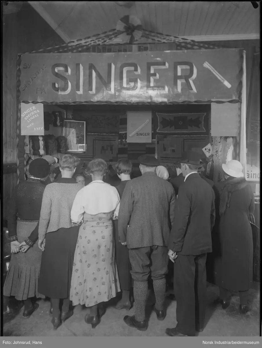 Handelsstevnet i Notodden 1933. Demonstrasjon og utstilling av Singer Symaskin, Skien. Mennesker samlet på utsiden av boden.