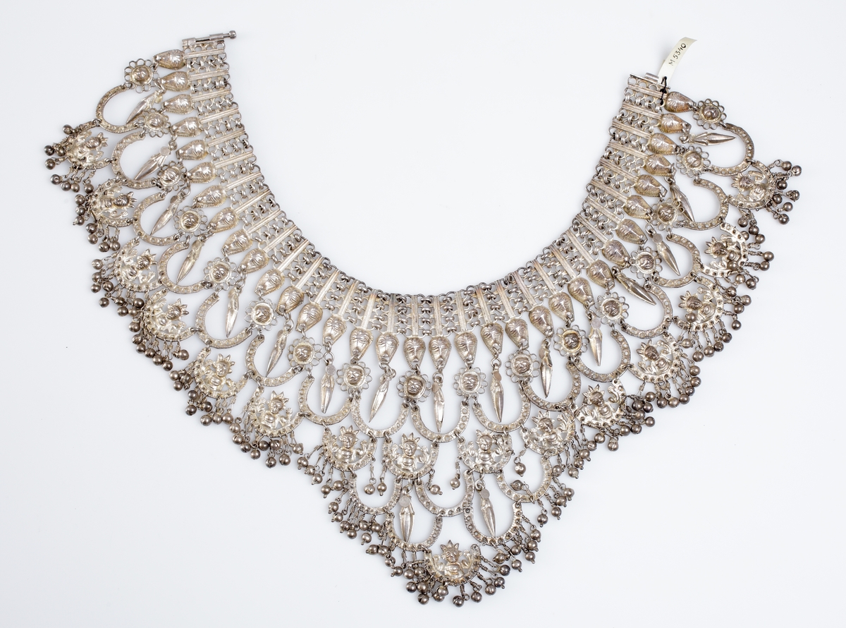 Halsband tillverkat av vitmetall i många sektioner. Det är i form av en halskrage dekorerad med djurhuvuden och olika hästskoformade länkar. 
Har tillhört sångerskan Christina Nilsson de Casa Miranda.

Inskrivet i huvudkatalog 1933.