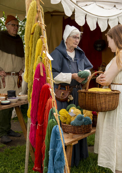 Kvinne i middelalderklær som forteller om garnfarging. Tau med hemper av hjemmefarget garn