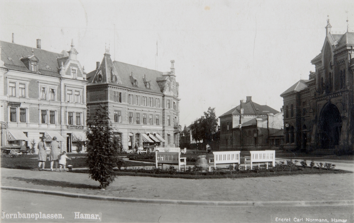Postkort, Hamar, Jernbaneplassen med beplantning, benker, bygården i Torggata 3 Ilsengs Cafe, Grand Hotell,
