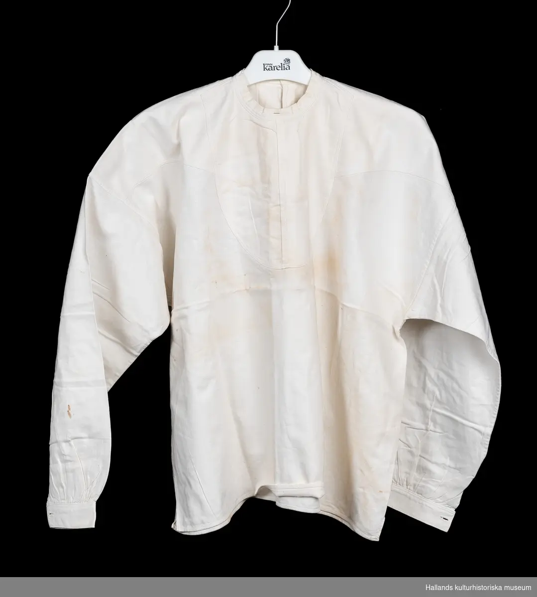 Skjorta av kypertvävd bomull, maskinvävd, maskinsytt. Lång ärm, fastsytt skjortbröst, slå med knäppning med två knappar baktill.
