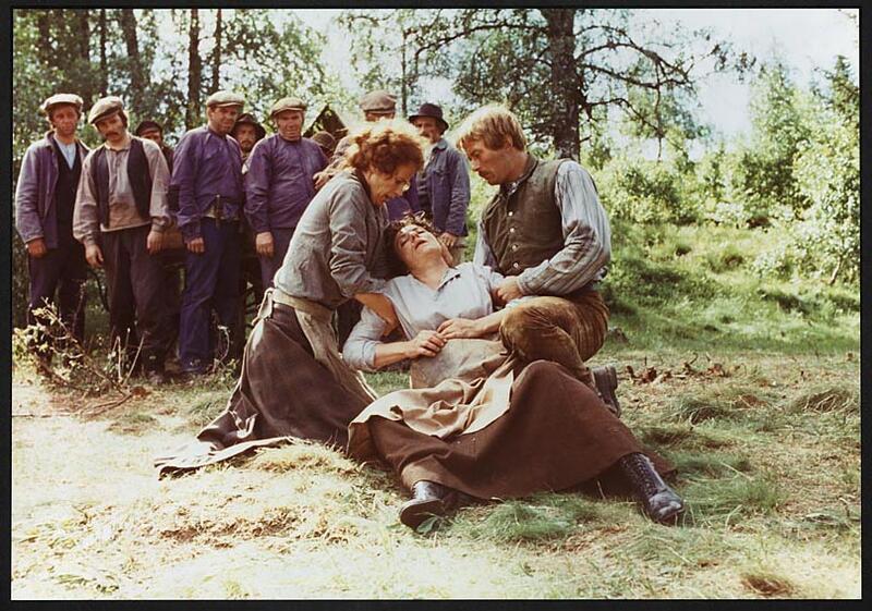 Foto fra filmen Rallarblod. En mann ligger skadet på bakken. På huk, på hver sin side, er en mann og en dame. Bak dem står en rekke menn og ser på.