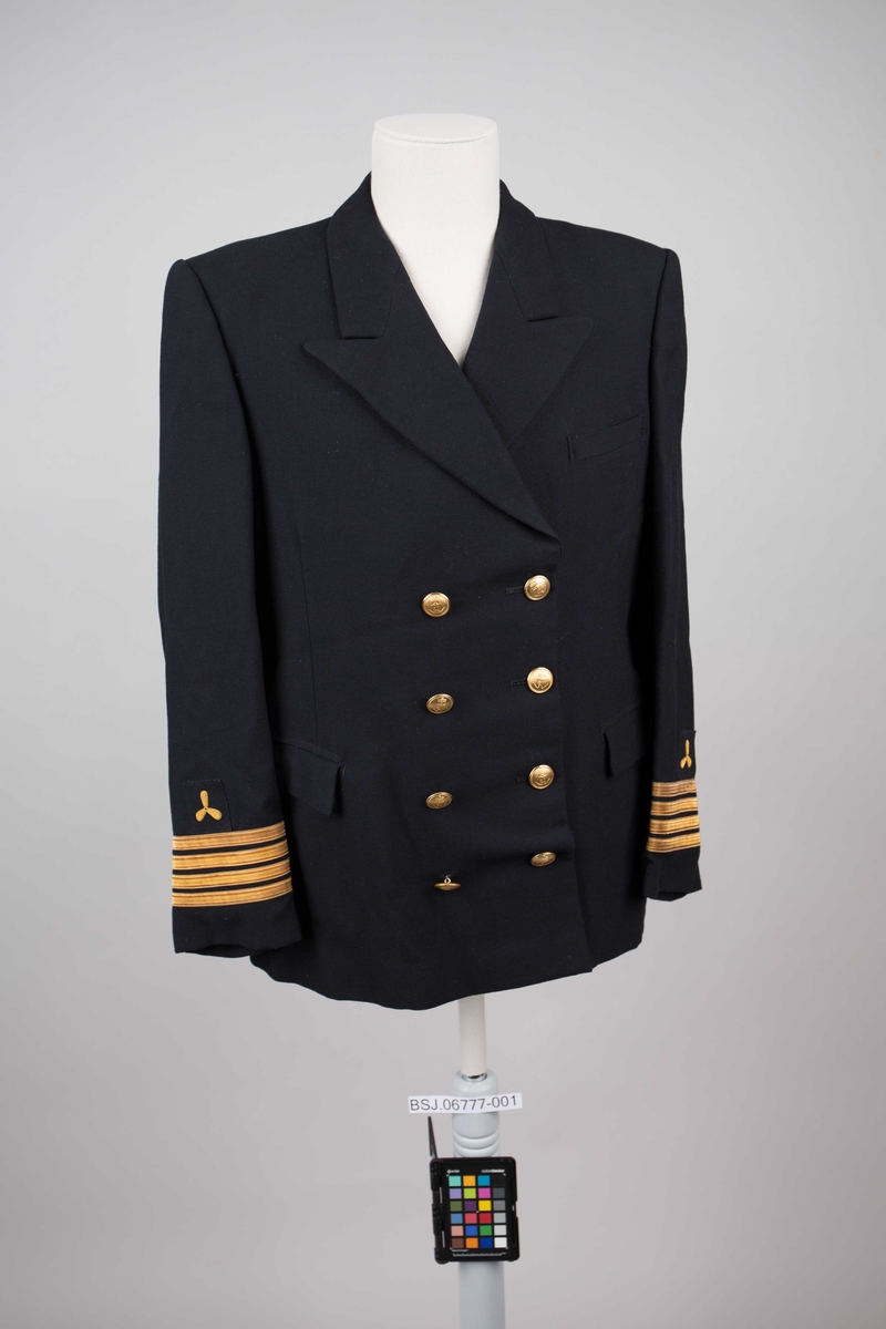 Maskinsjef uniformsjakke med påsydde distinksjoner på erme (4 stk. gullbånd og brodert propell). Dobbelspent med til sammen 8 stk. knapper i gullfarge med motiv av anker.