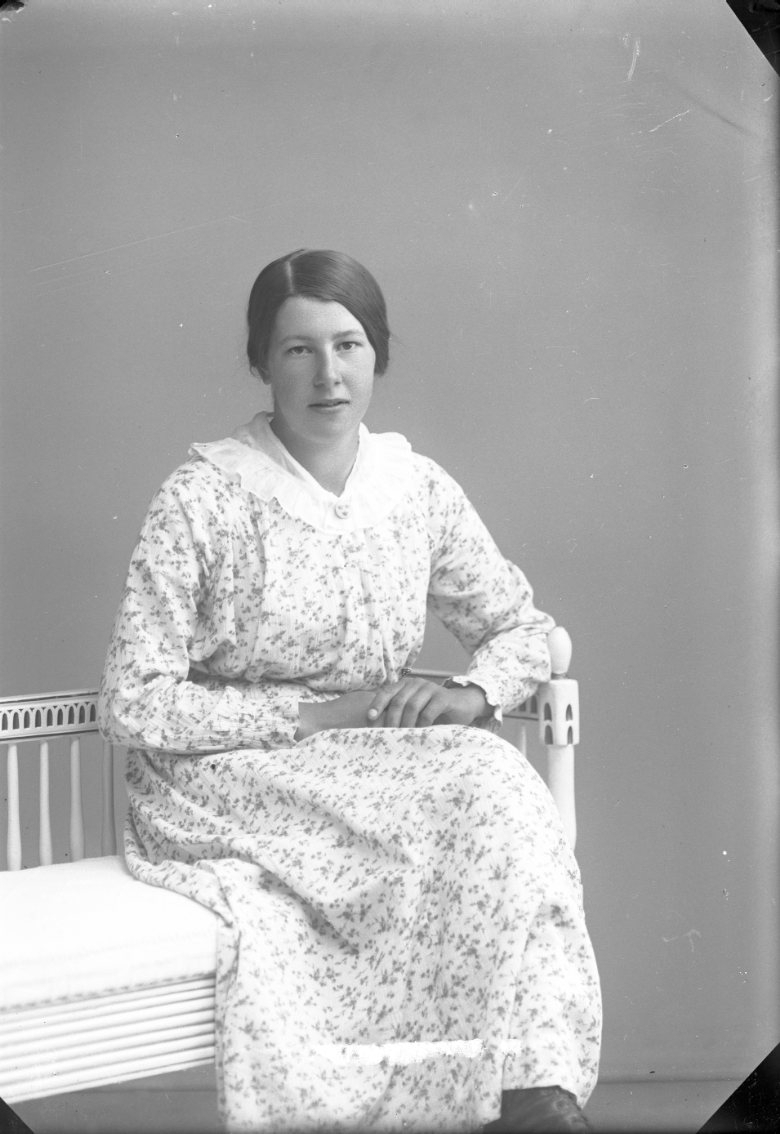 En ung kvinna i blommig klänning sitter i fåtölj.