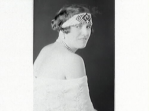 Porträtt av Florence Hansson, iförd ett brett, mönstrat pannband och pärlhalsband.