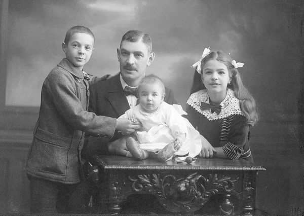 Ateljébild av handelsman Oscar Pehrson med barnen Håkan, Greta och bebisen Sven på bordet.