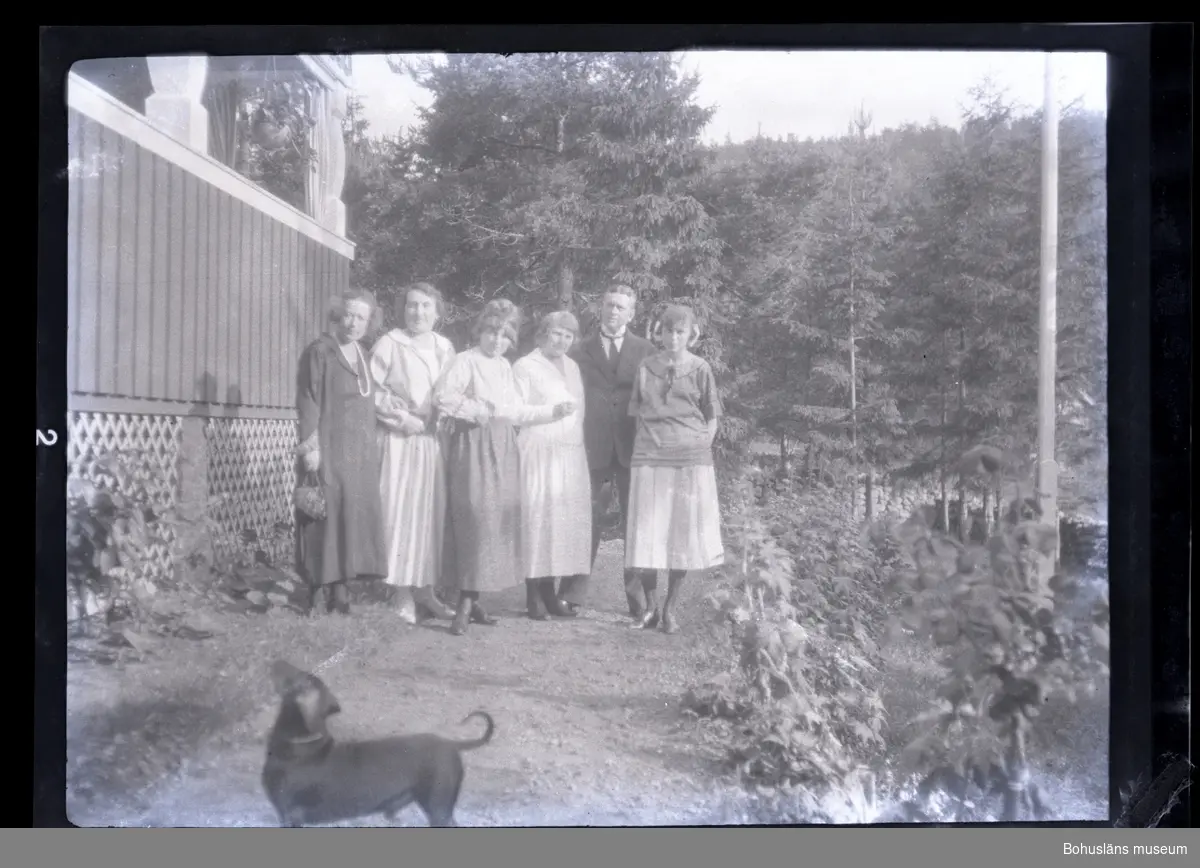 Sex personer står framför ett hus med skog omkring. En hund står i förgrunden.