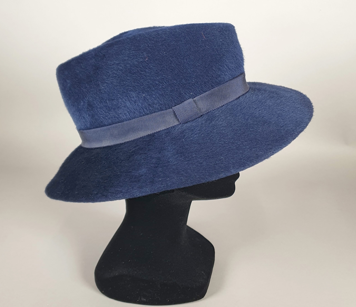 Blå hatt av børstet ull, med bred brem og blått ripsbånd rundt pullen. Blått ripsbånd på innsiden.