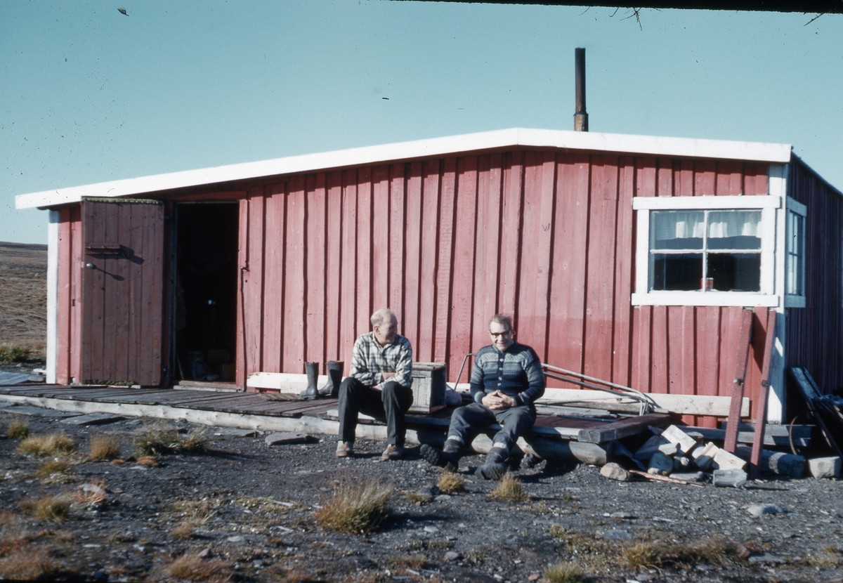 To personer sitter utenfor hytte. Bilde fra Bjørnar Nilsen, sønn av stiger Johannes Nilsen Støpseth som kom opp i 1948 og var her i 40 år.
