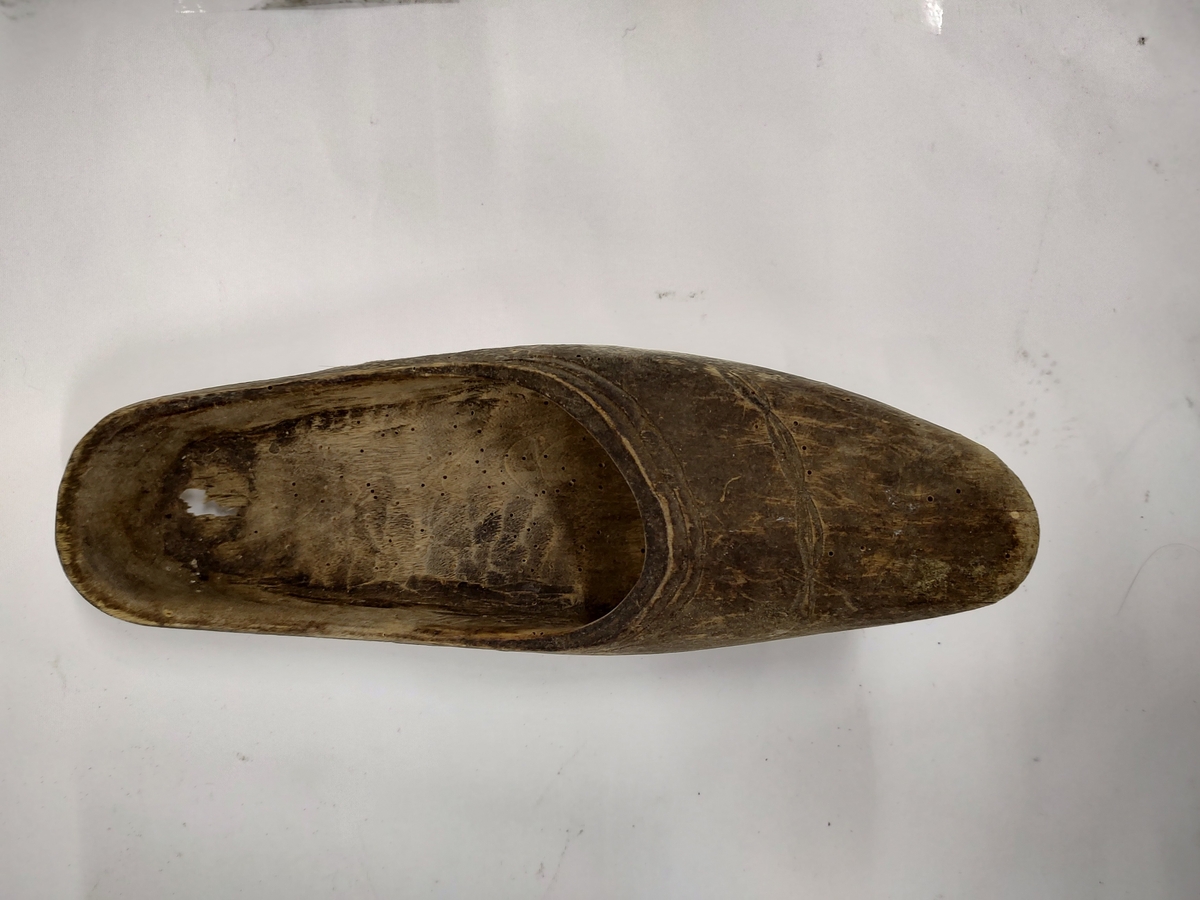 Tresko uten hæl, skåret til og hult ut av et trestykke. Malt svart. Det er skåret inn et dekorativ mønster foran på skoen.