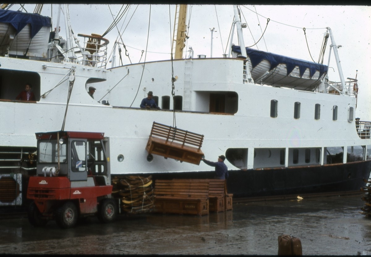 Benker til oppbevaring av redningsvester på dekk heises ombord i hurtigruteskipet MS Vesterålen (1950). På kaia ligger flere dekkstoler klar til å heises ombord 